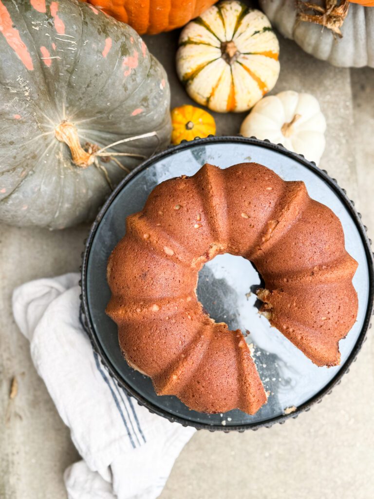 Overhead view of a golden-brown Toffee Coffee Cake baked in a bundt pan, surrounded by colorful fall pumpkins.